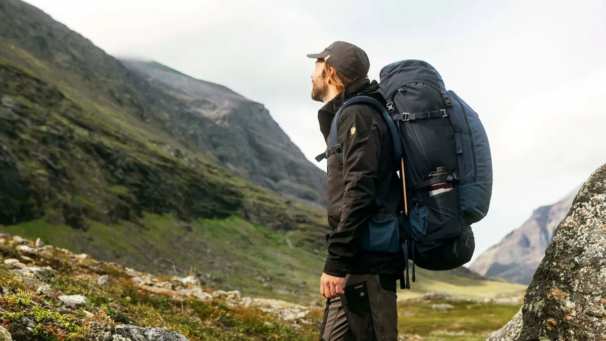 Vandrare med packad ryggsäck blickar ut över en fjälldal på väg mot lägerplatsen
