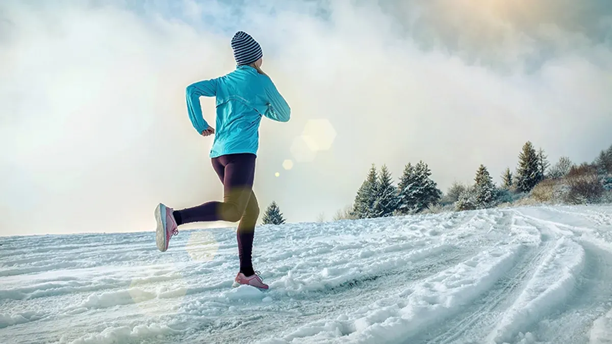 Löpare i turkos jacka och tights springer på en snötäckt väg i vinterlandskap