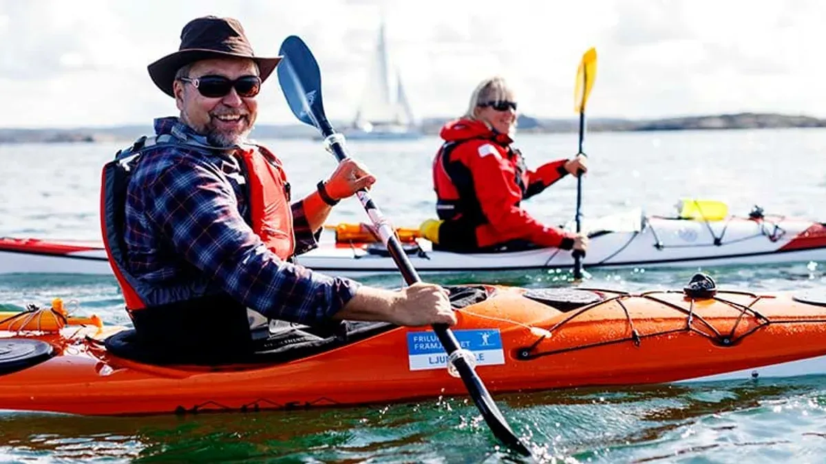 Två kajakpaddlare i öppet vatten med segelbåt i bakgrunden