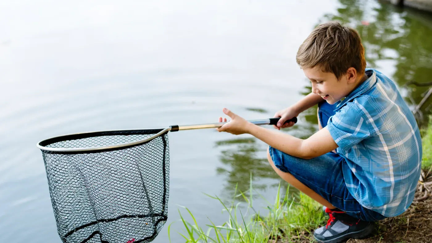 Pojke som håvar upp en fisk med en teleskophåv vid vattenkanten