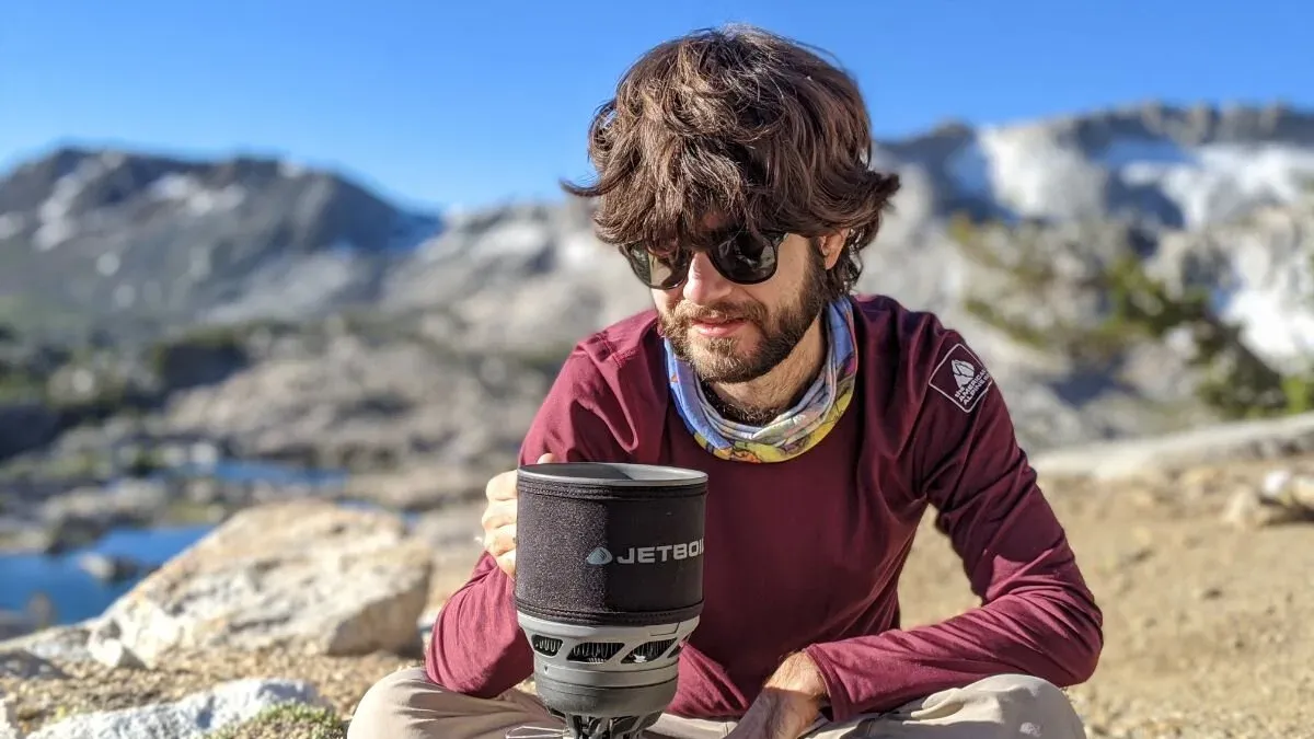 Vandrare håller i ett Jetboil-stormkök och lagar mat sittande vid en fjällsjö