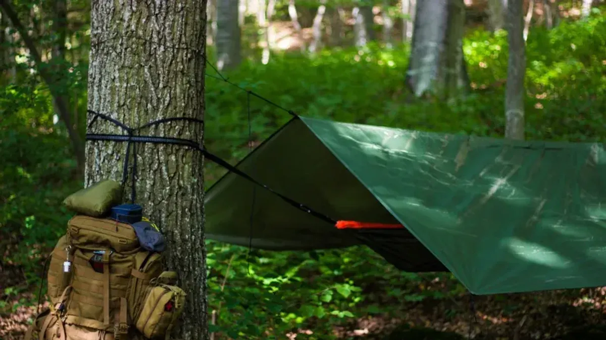 Uppackad bug out bag i militärgrönt med anteckningsblock, tältstänger och första hjälpen-märke synligt