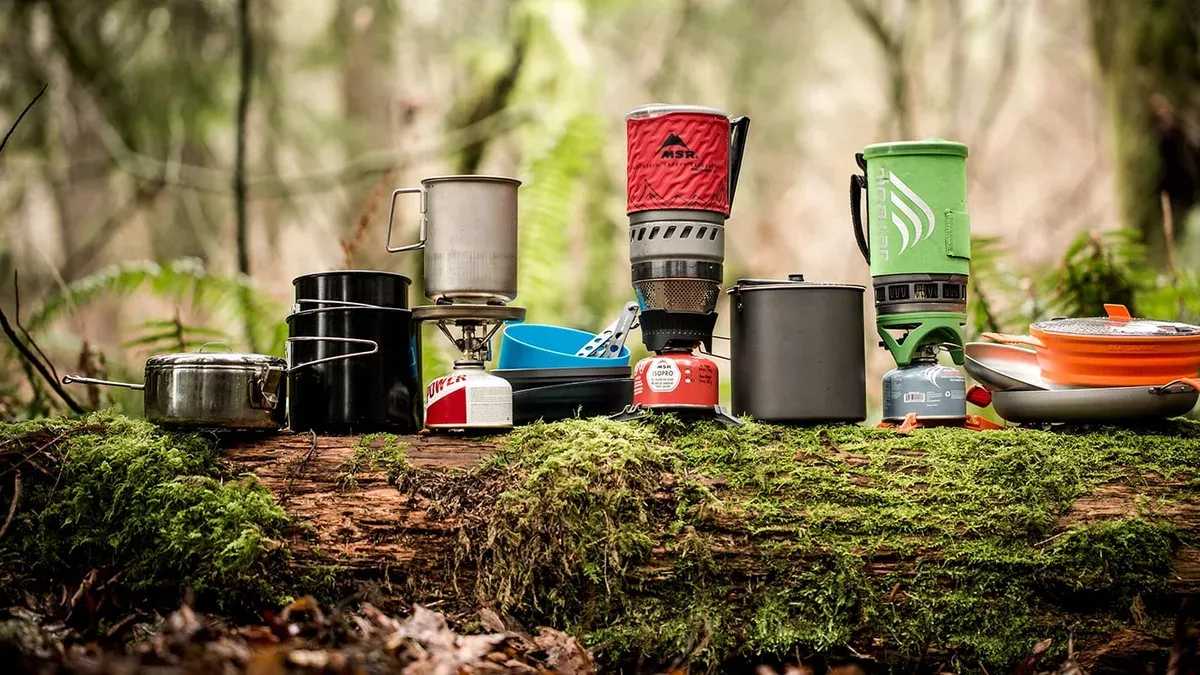 Olika stormkök och campingkokkärl uppradade på en mossbelagd stock i skogen