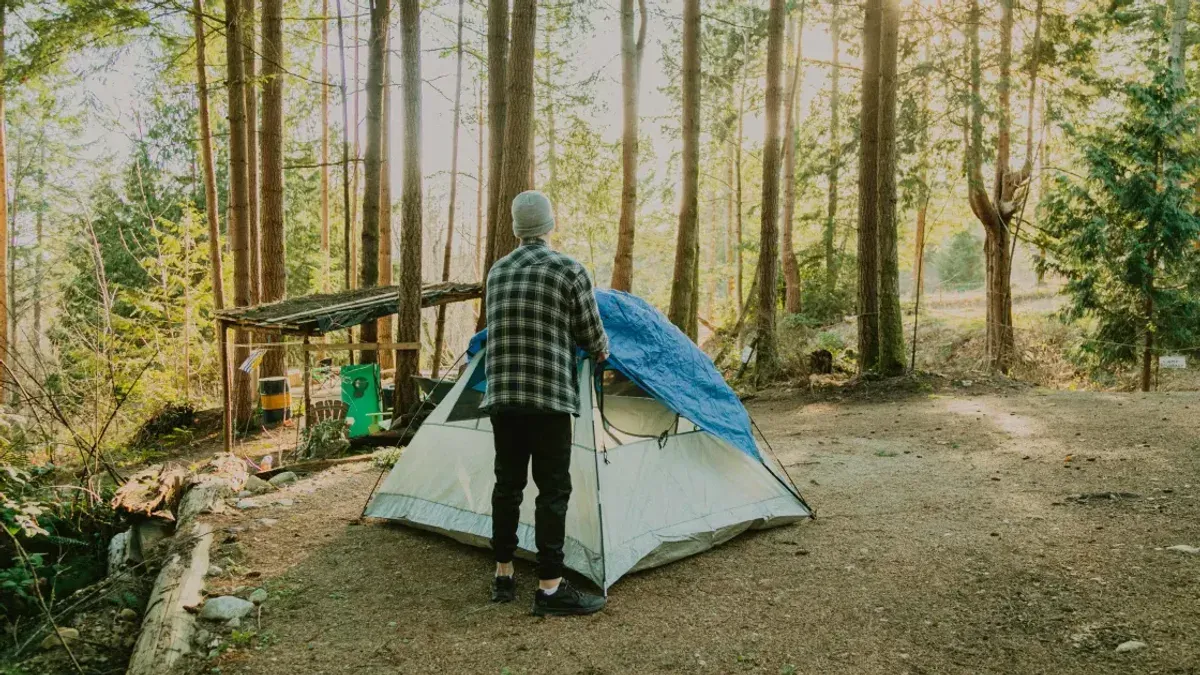 Person står vid ett tält i skogen på en enkel campingplats