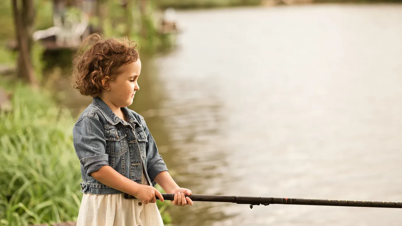 Flicka som håller i ett fiskespö vid vattnet en sommardag