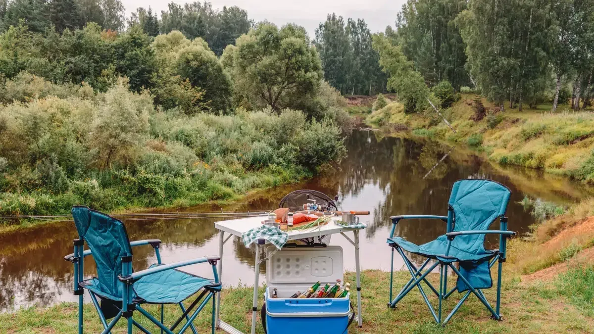 Campingstolar och campingbord uppställda vid en å i skogen