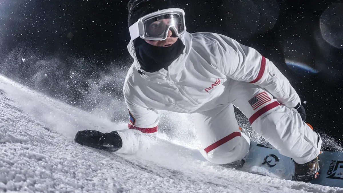 En snowboardåkare i en vit vintersportoverall med röda detaljer i en tävlingssvängning på natten