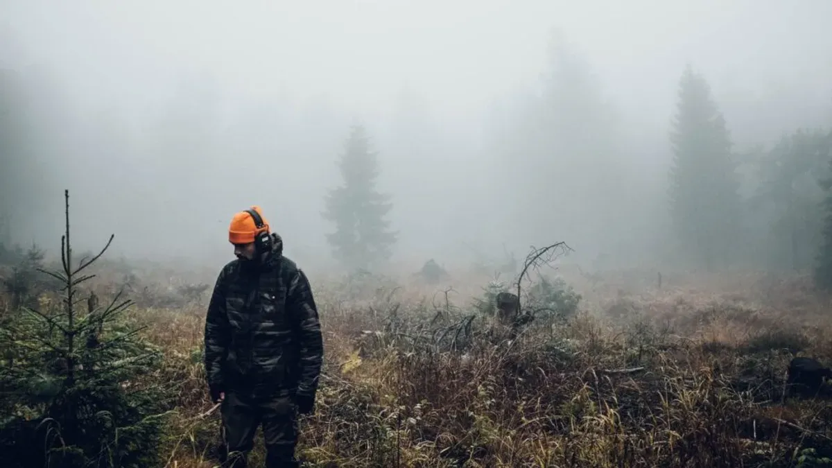 Jägare i kamouflage med orange mössa i dimmig skog