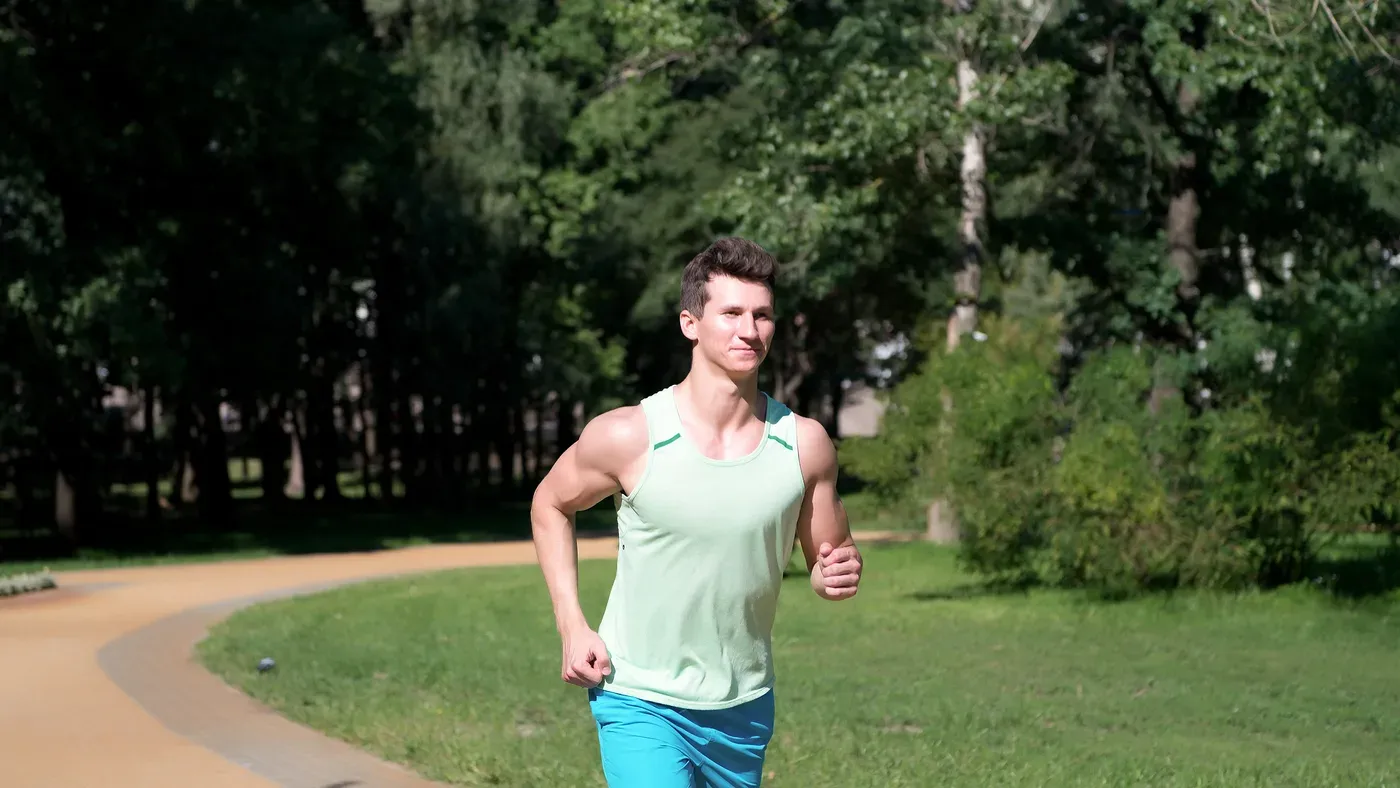 Löpare med upprätt hållning joggar på en gångväg genom en grön park
