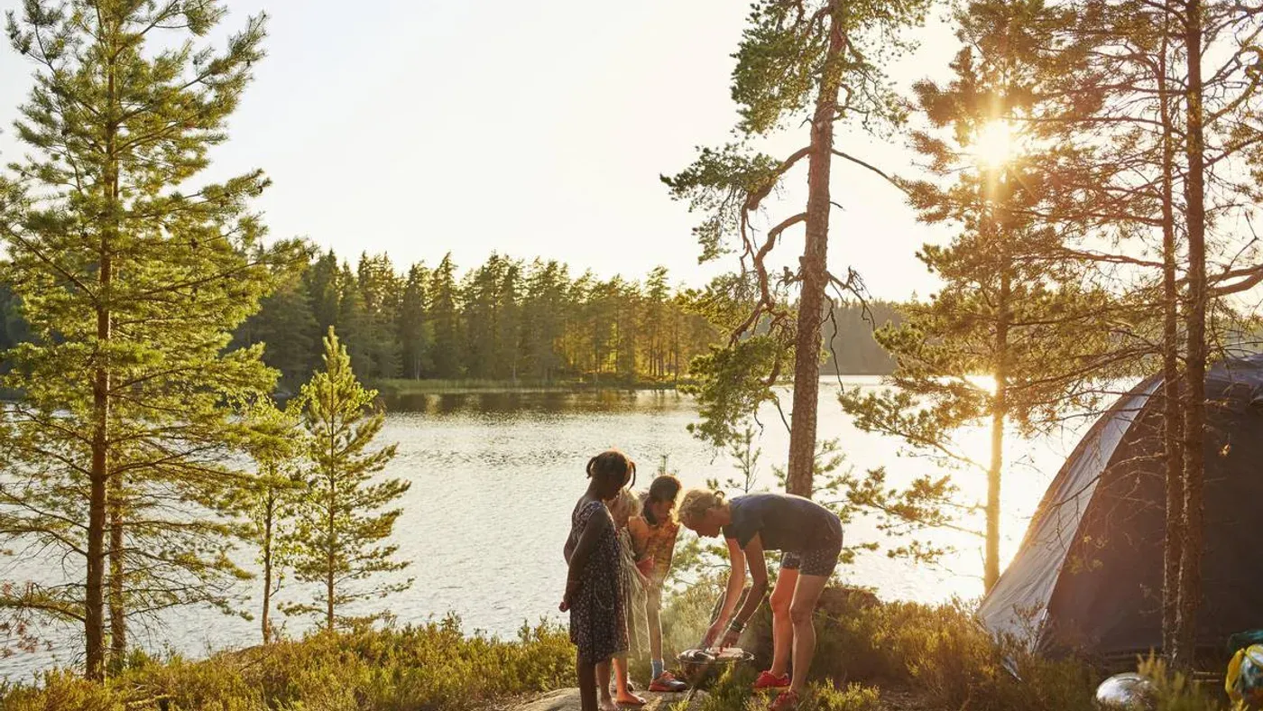 Familj vid tältplats i solnedgång vid en sjö i skogen