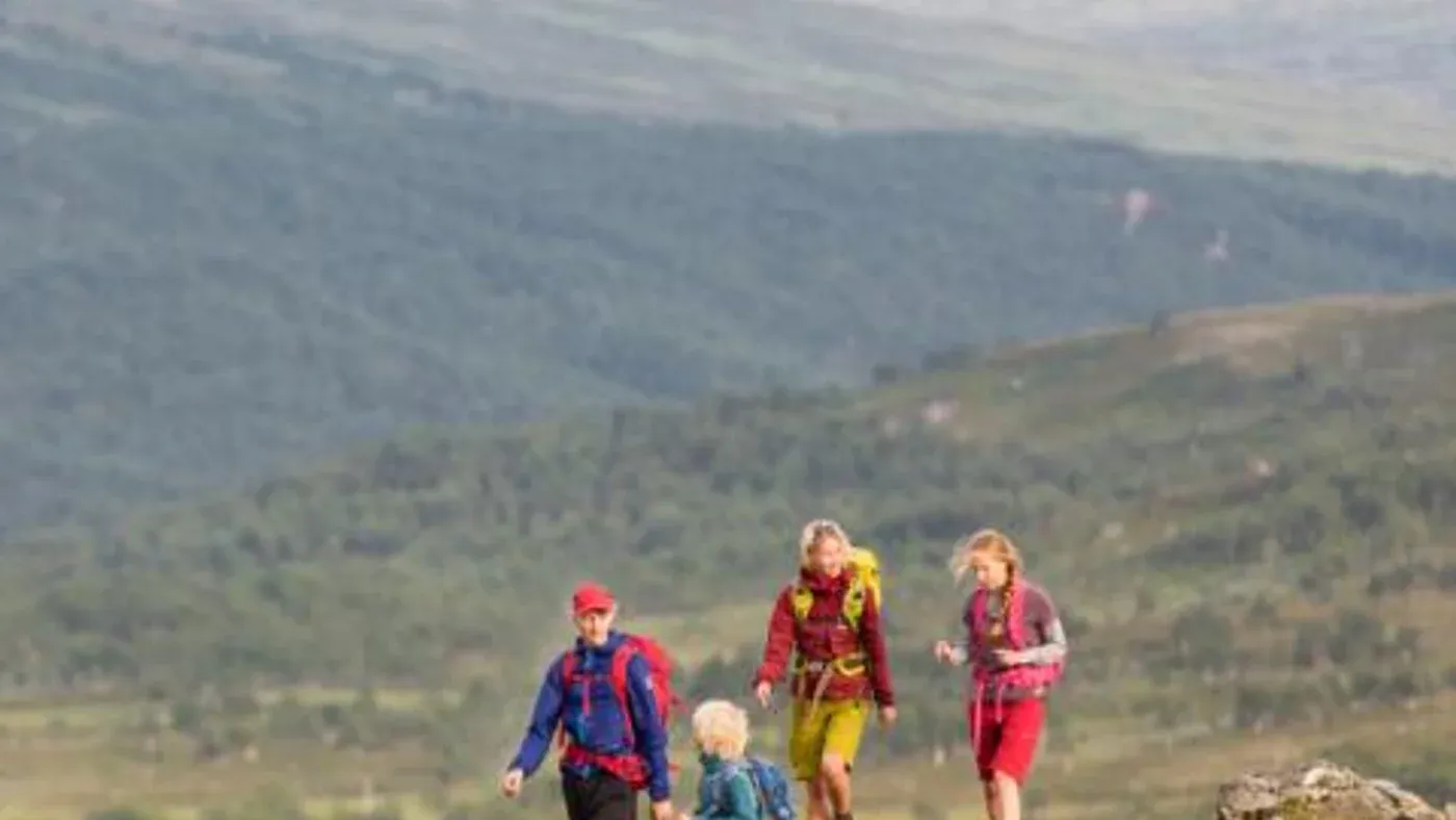 En familj med fyra medlemmar vandrar på en fjällstig med utsikt över dalen