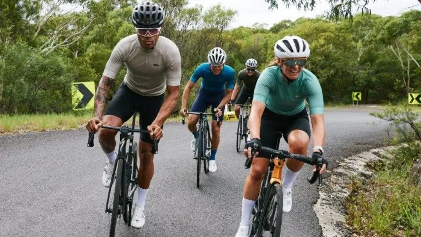 Grupp cyklister i cykeltröjor och hjälmar på landsväg omgiven av grönska
