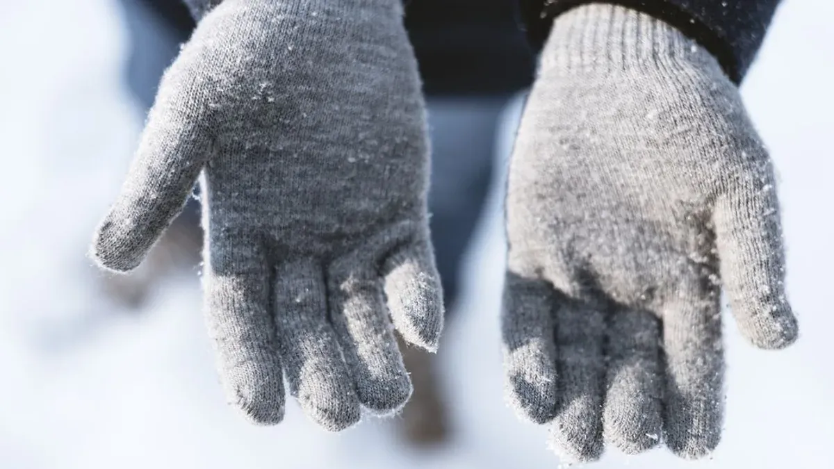 Närbild på stickade grå vantar i snö