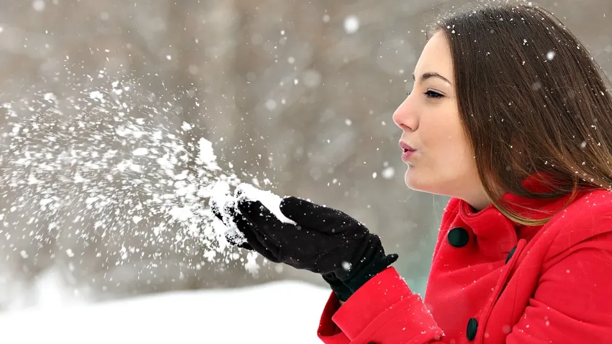 Kvinna i röd jacka blåser snö från svart handske