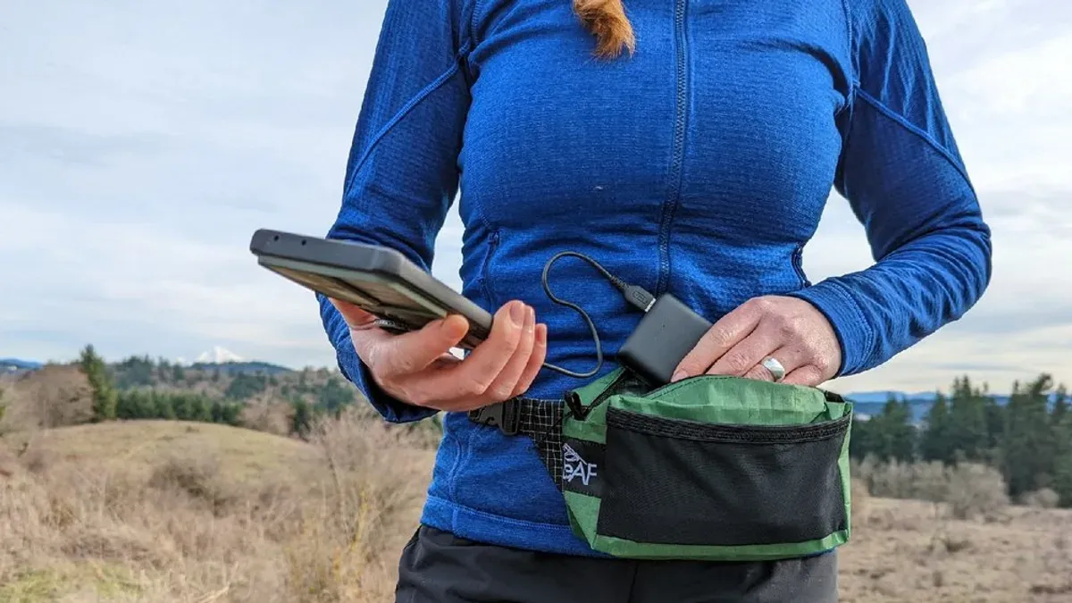Kvinna laddar telefon med powerbank ur grön midjeväska