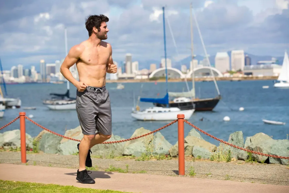 Barbröstad man joggar längs hamnpromenad, kalsonger ej synliga