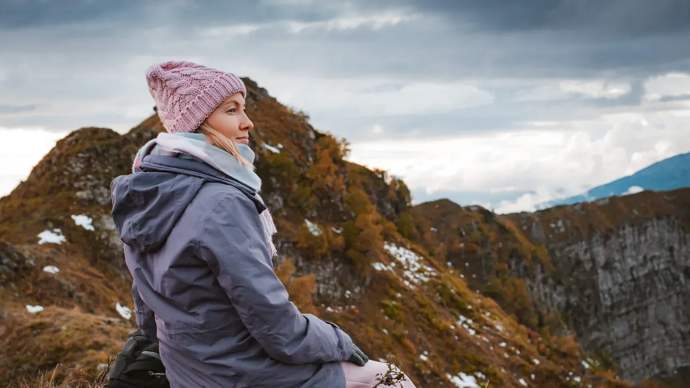 Kvinna i lila skaljacka och mössa på klippig bergstopp