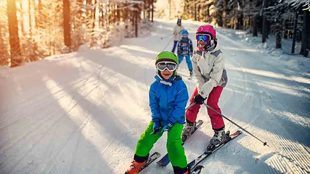 Två barn på skidor i grön och rosa hjälm i skog