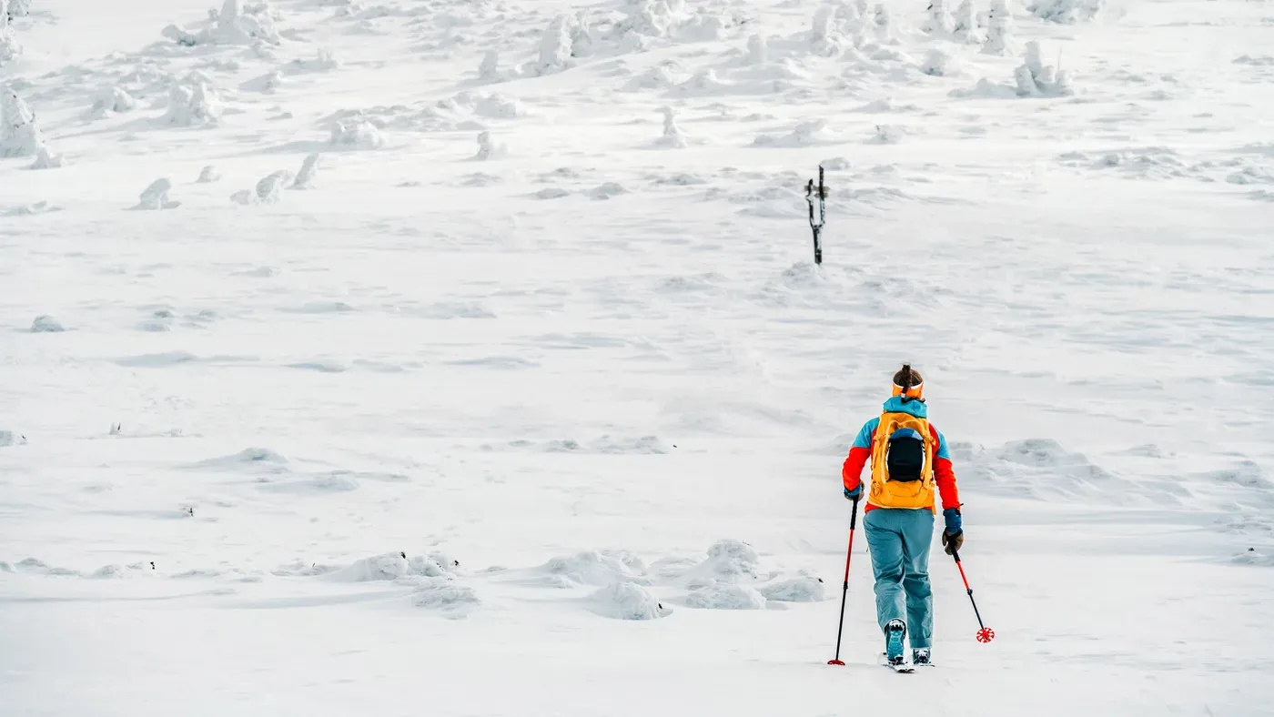 Skidåkare med ryggsäck vandrar över öppet snöfält