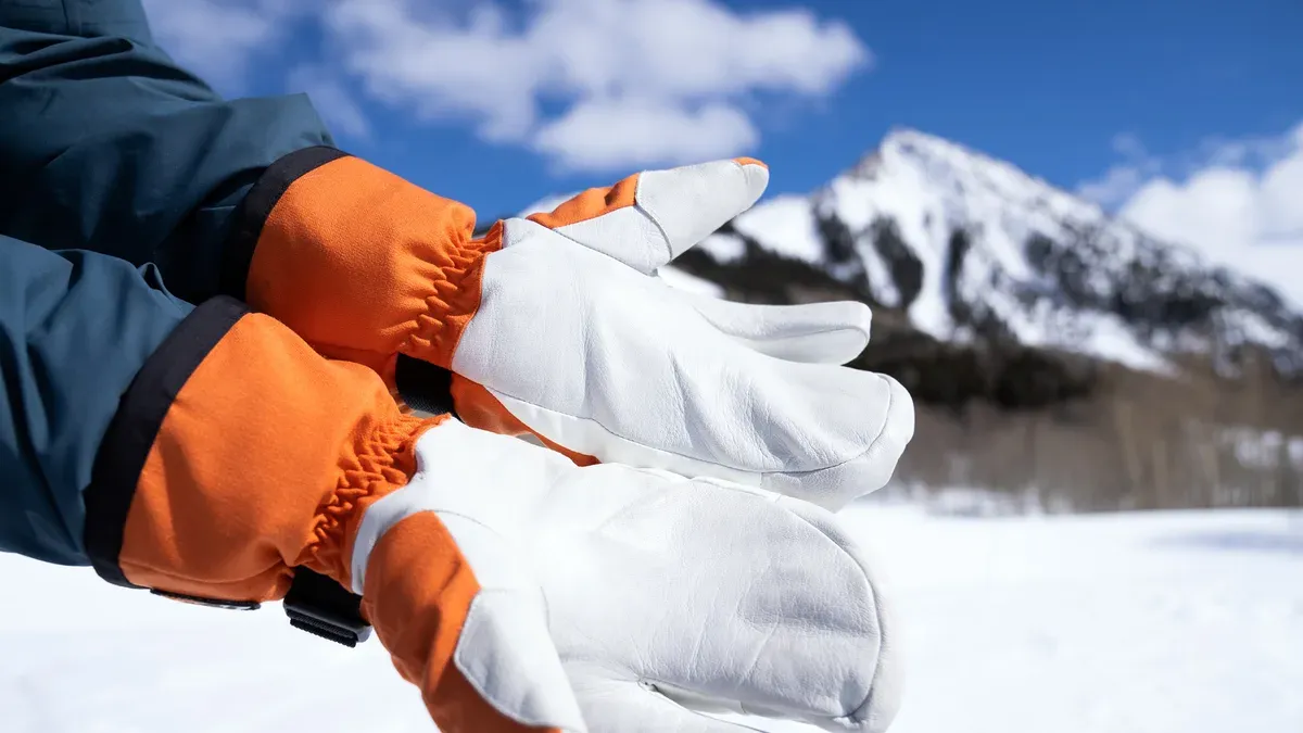 Vita och orange skinnvantar mot snötäckt fjäll