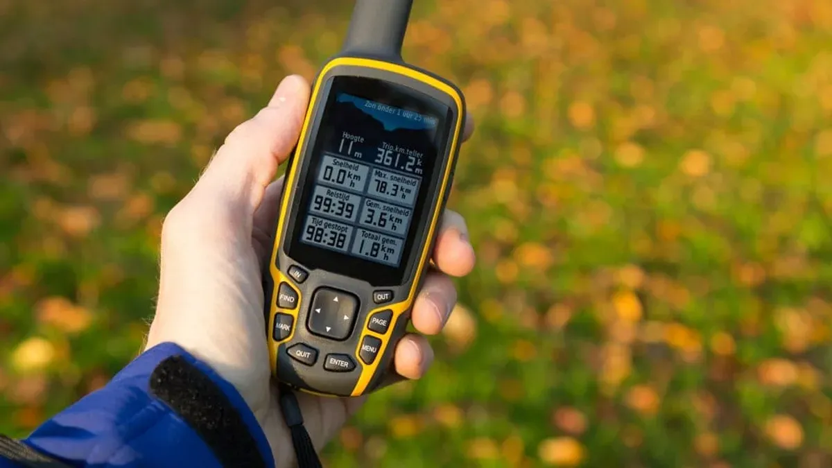 Hand håller upp GPS med mätdata mot höstlöv