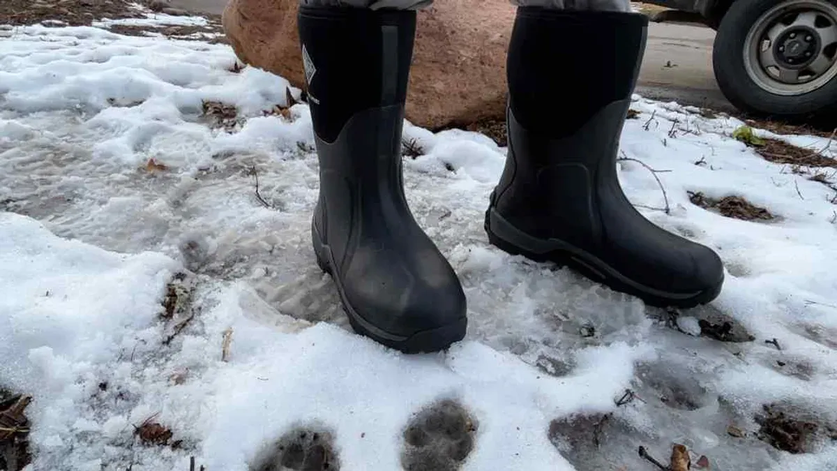 Svarta fodrade stövlar på snöig gårdsplan bredvid stenblock