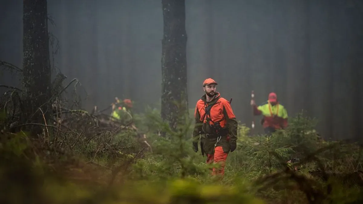 Jägare i orangea kläder i dimmig skog under jakt