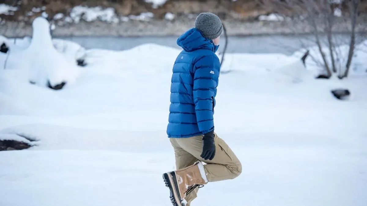 Person i blå jacka och bruna vinterkängor går i snö