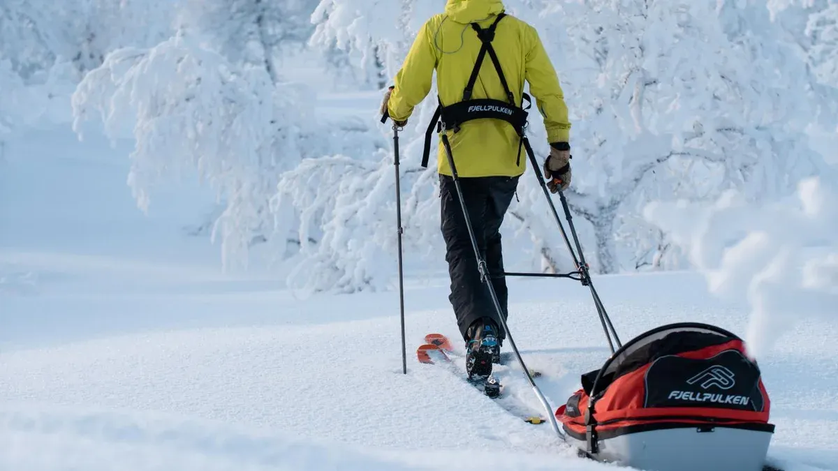 Skidåkare drar röd Fjellpulken-pulka genom snöig skog