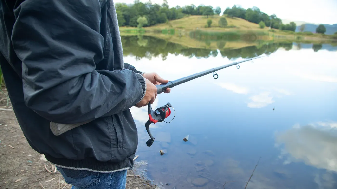 Man håller fiskespö med haspelrulle vid sjö