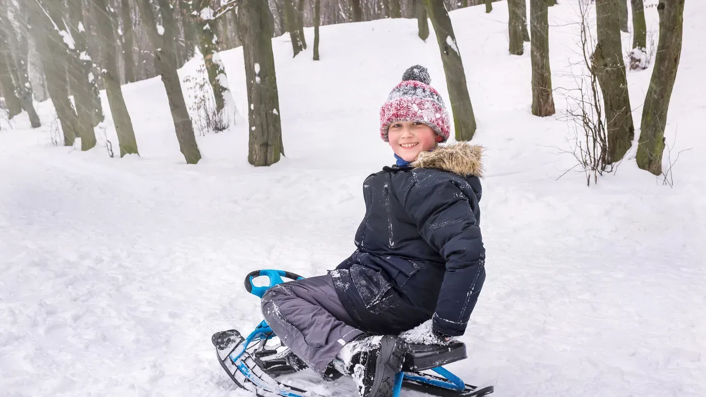 Barn i vinteroverall åker pulka i snötäckt skog