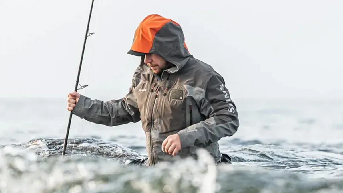 Fiskare i orangehuvad jacka vadar i havsvågor med spö
