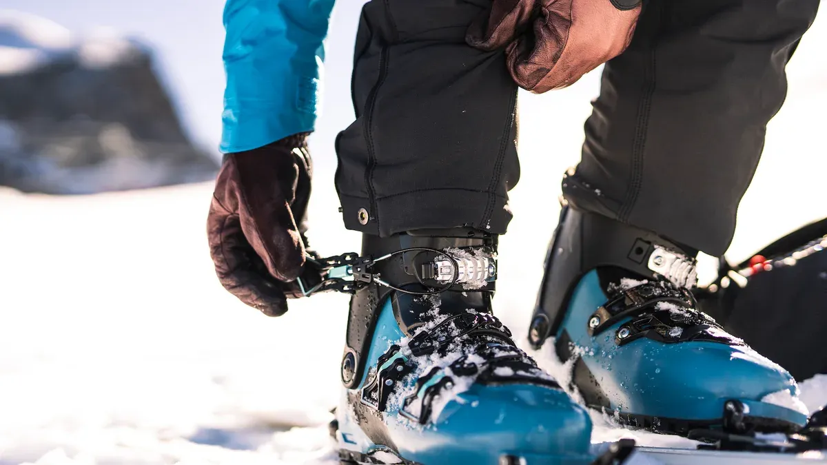 Person spänner turkosa pjäxor stående på skidor