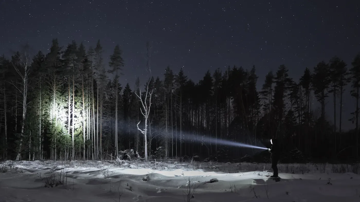Person lyser med pannlampa mot skog i vintermörker