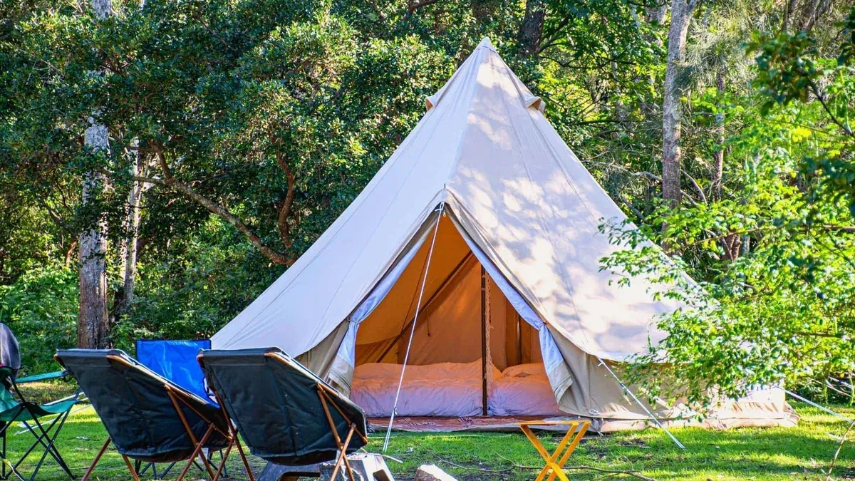 Stor beige tältkåta bland träd med campingstolar utanför