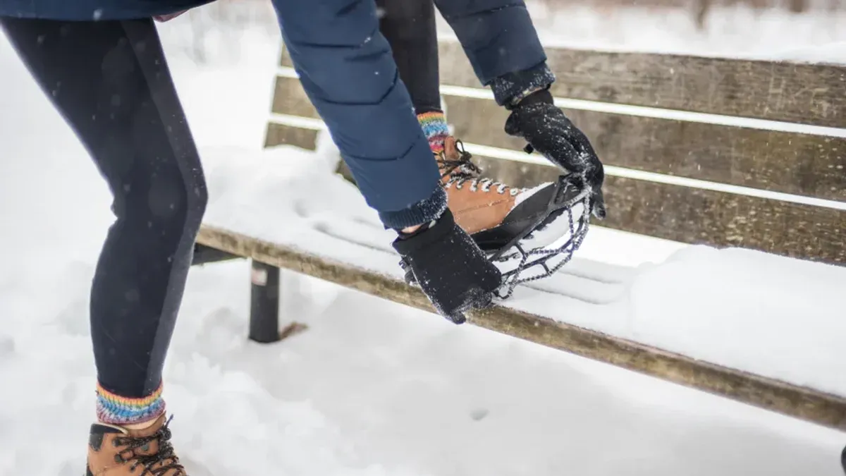Personer sätter på broddar stående vid snötäckt bänk