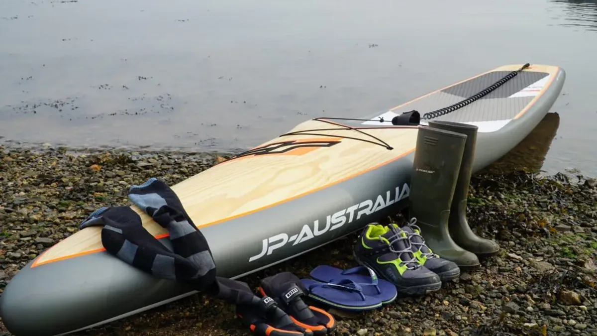 SUP-bräda och badskor på stenig strand