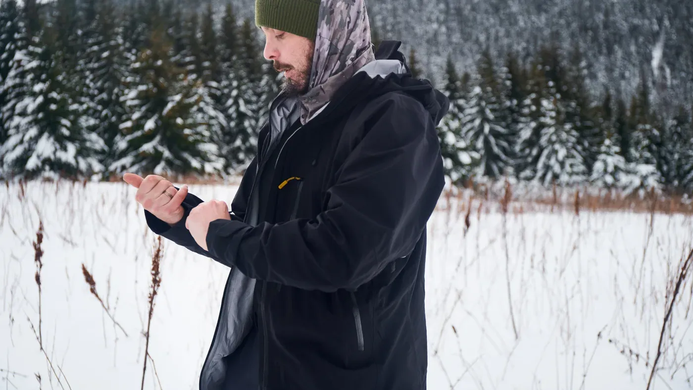 Man i svart jacka justerar ärmen i snötäckt skogsmiljö