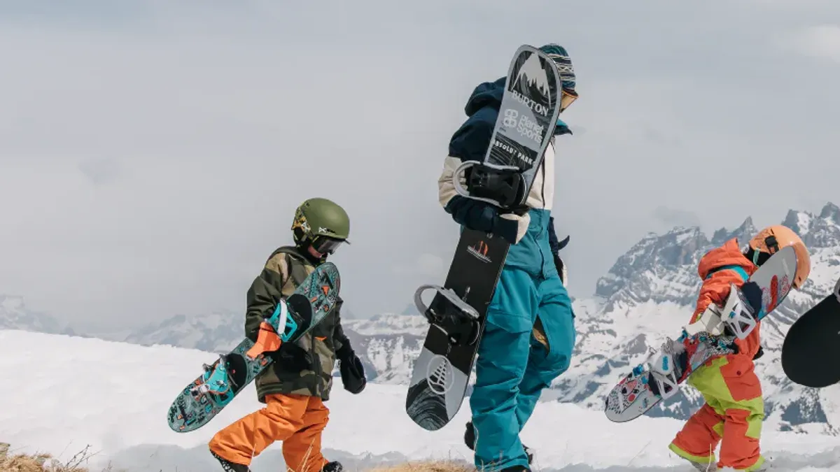 Barn bär snowboards i orange och blå skidbyxor på fjäll
