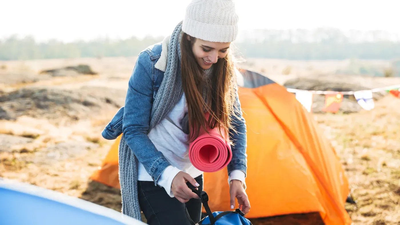 Kvinna packar campingmadrass i blå packpåse vid tält