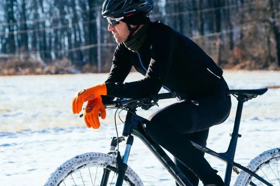 Cyklist i orange vinterhandskar lutar sig mot styret i snö