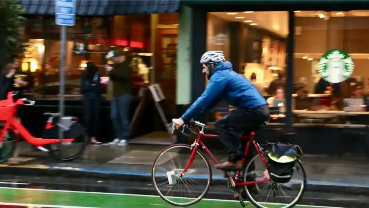 Cyklist med cykelväska kör förbi butik på stadsgata