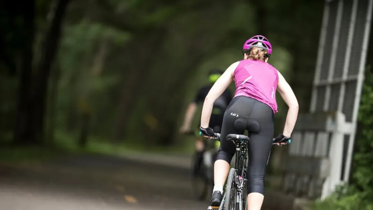 Cyklist i rosa tröja och svarta cykelbyxor på skogsväg