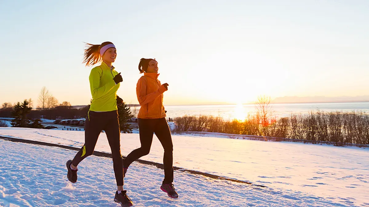 Två kvinnor joggar i snölandskap vid solnedgång