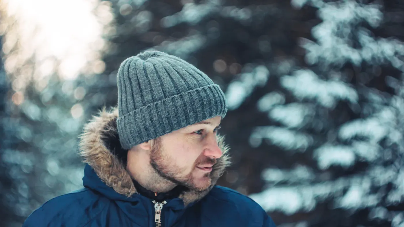 Man i grå mössa och blå parkas i snöig skog