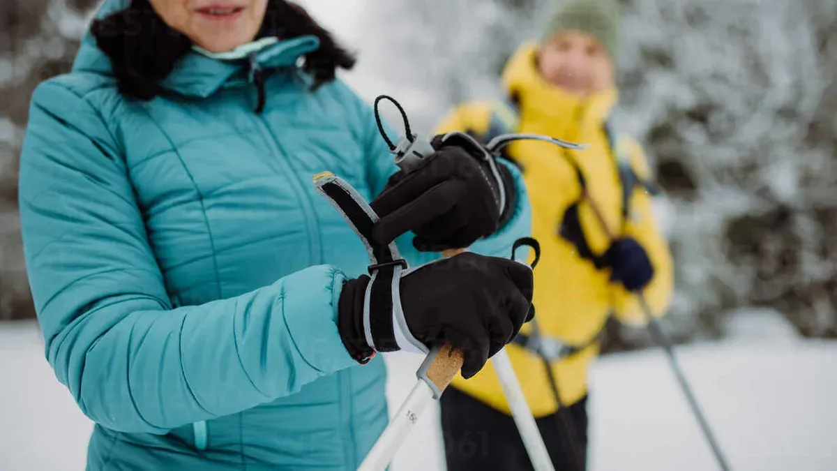 Man justerar grå skaljacka med röda dragkedjor på fjäll