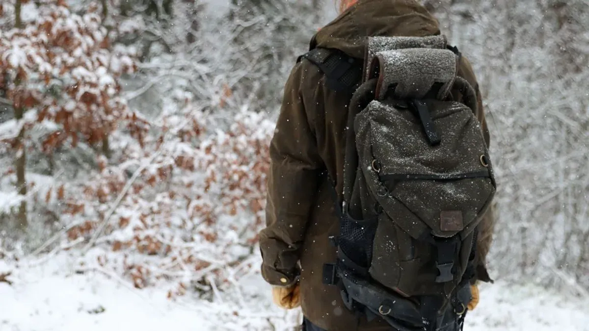 Person bär stolryggsäck på ryggen i snöigt skogsväder