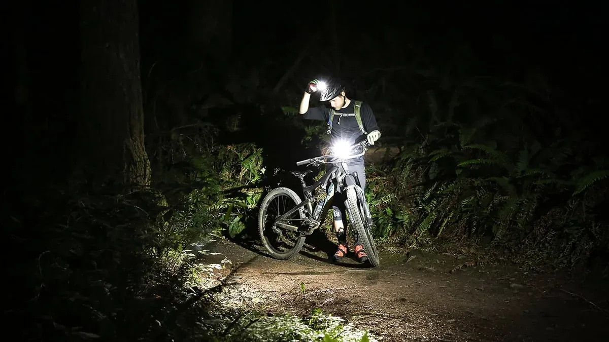 Mountainbikecyklist med tänd hjälmlampa i mörk skog
