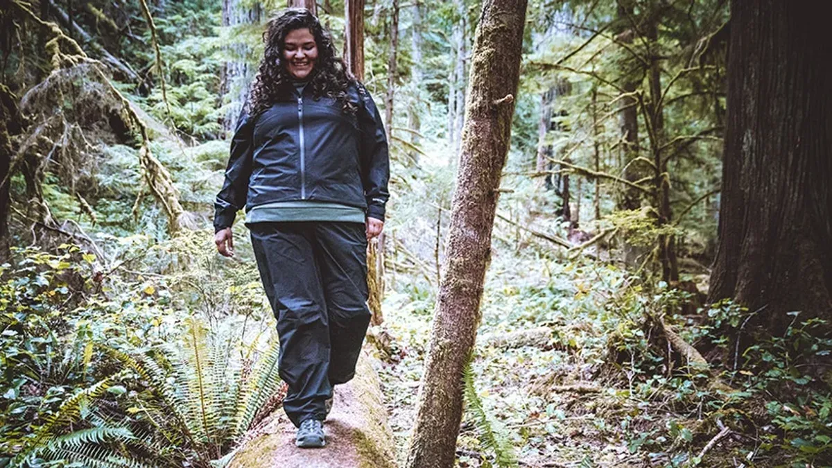 Leende kvinna i mörkblått regnställ går på stig i skog