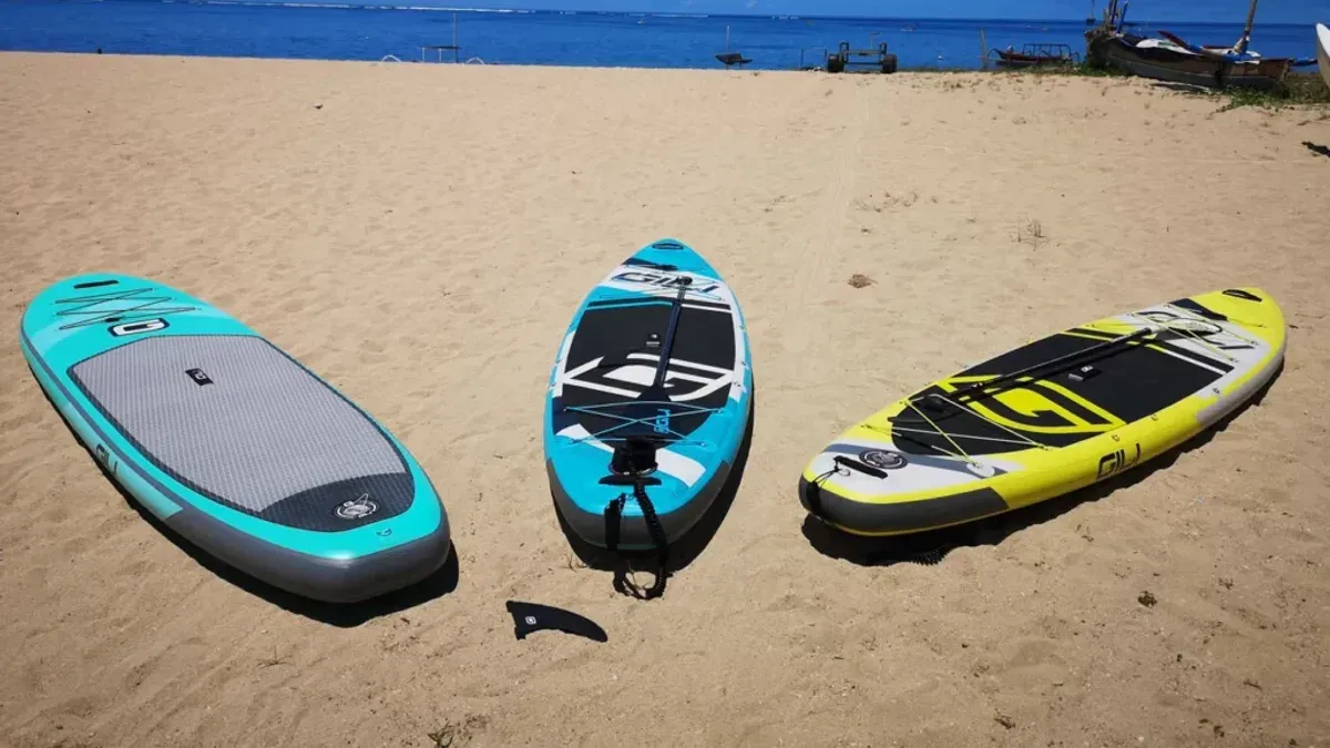 Tre uppblåsbara SUP-brädor liggande på sandstrand